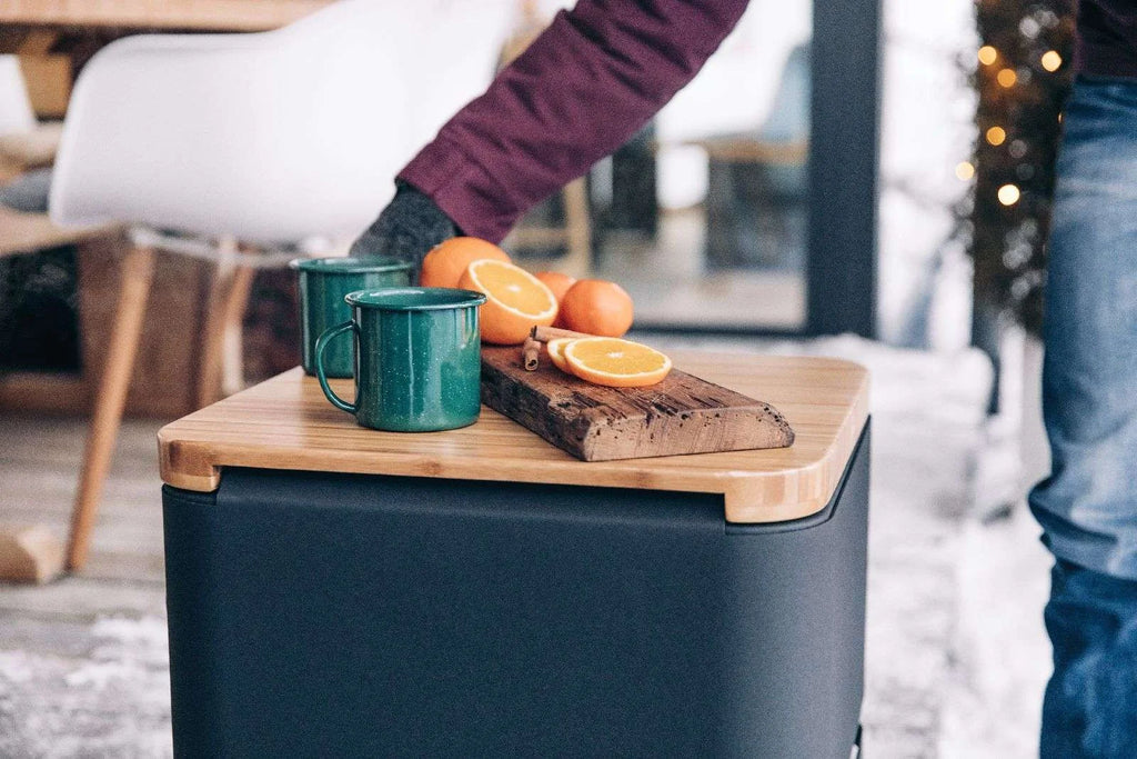 Ottoman de rangement bleu marine et noir avec dessus en bois, tasses vertes, oranges sur planche à découper.