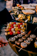 Grill de barbecue avec brochettes et champignons, tomates, tranches de fromage, rondelles de pain et légumes dessus.