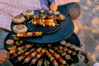 Plateau de service noir à étages avec brochettes colorées et assiettes pour les rassemblements en extérieur.