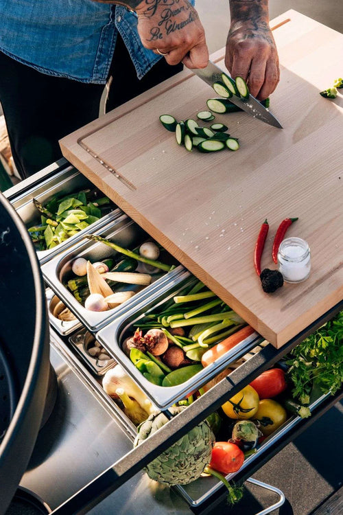 Planche à découper en bois avec des concombres tranchés et des piments rouges.