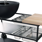 Gril-barbecue en acier inoxydable avec accents noirs et une planche à découper en bois sur le côté.
