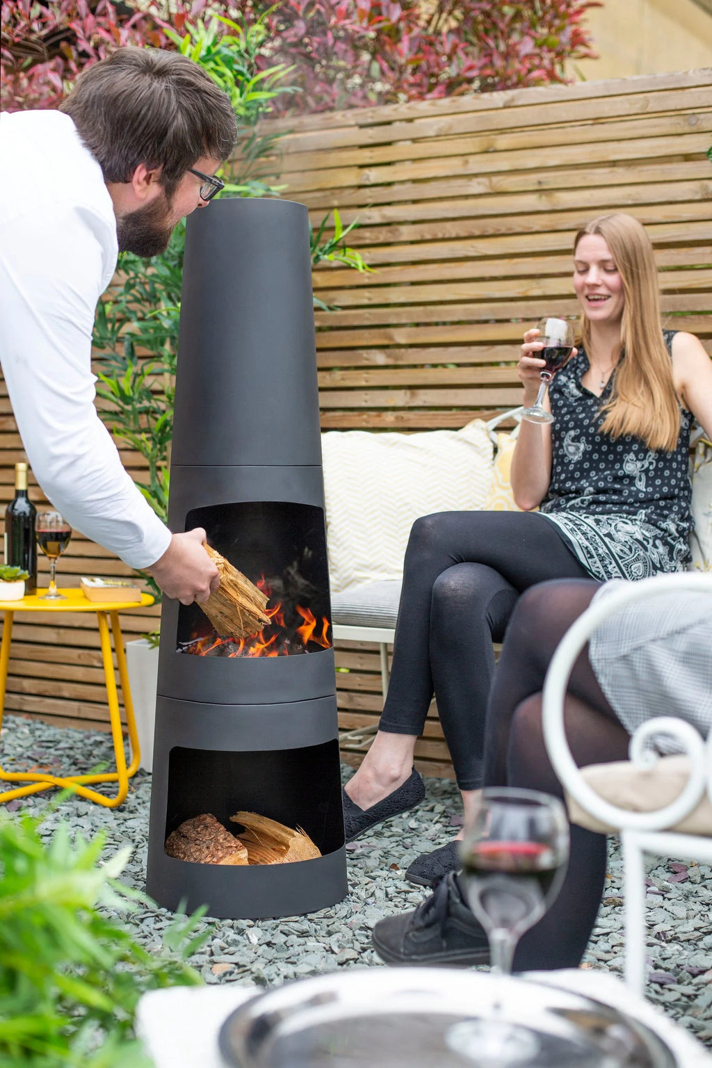 Cheminée extérieure cylindrique noire avec compartiments empilés pour le bois et flammes visibles à l’intérieur