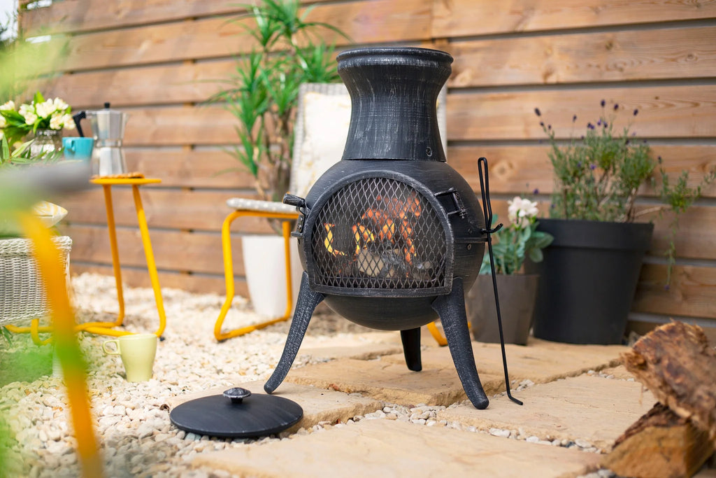 Chiminea en fer forgé noir avec un devant en maille et des pieds trépied, dotée d’un corps arrondi et d’un haut évasé.