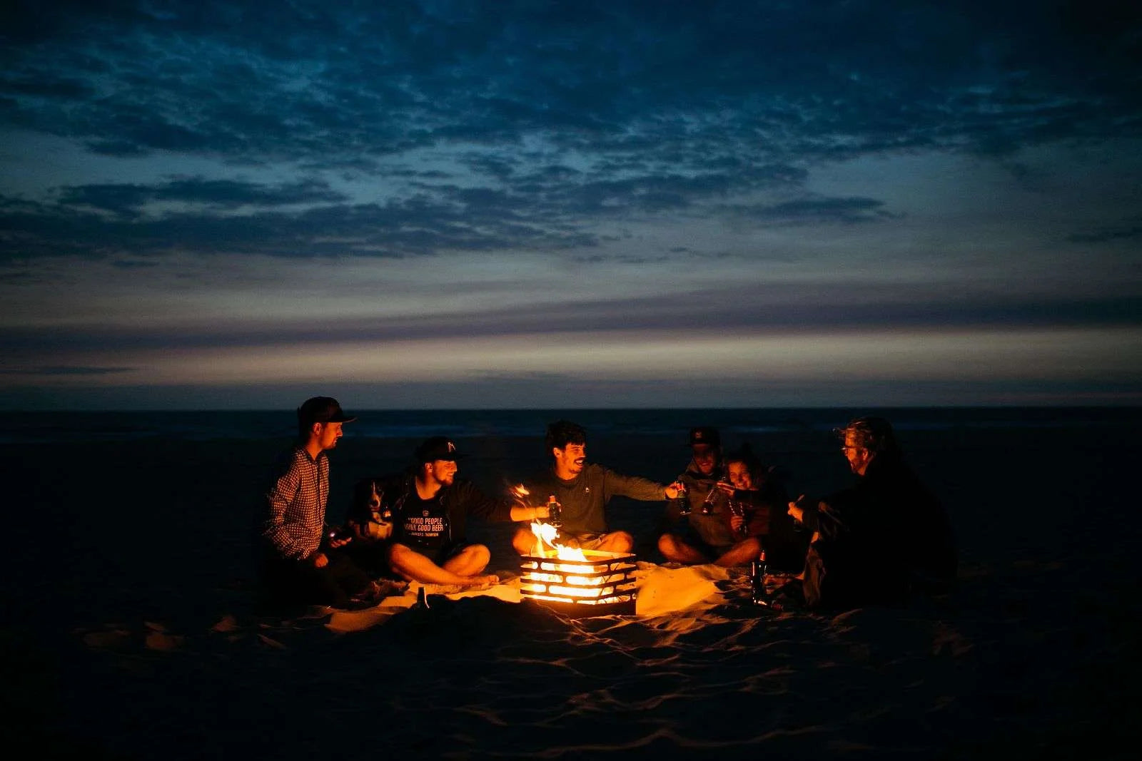 Feu de camp avec des braises luisantes et des flammes crépitantes, projetant une lueur orange chaude sur le sable environnant.