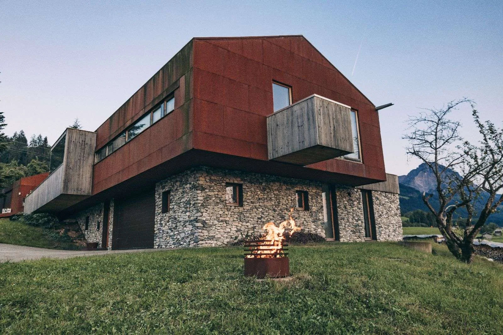 Maison en métal ondulé rouge avec accents en pierre et balcons en bois.
