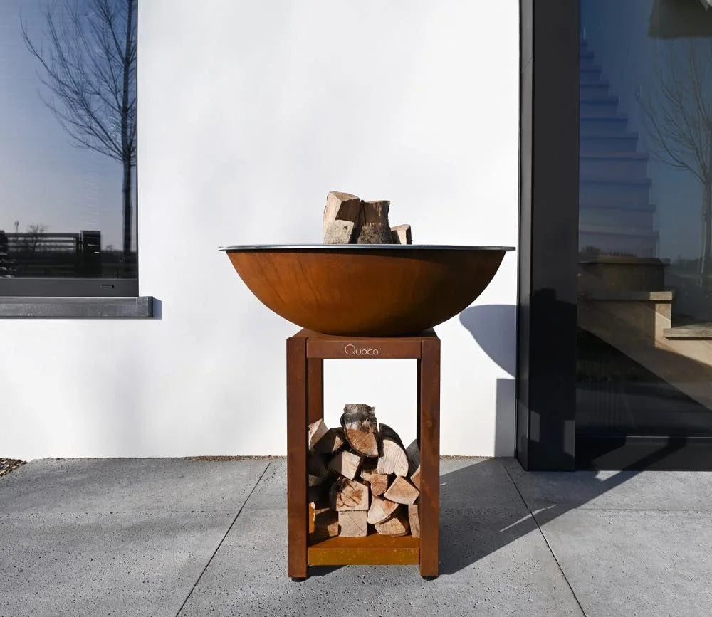 Bol en cuivre rouillé de style rustique avec un support en bois tenant des bûches empilées.