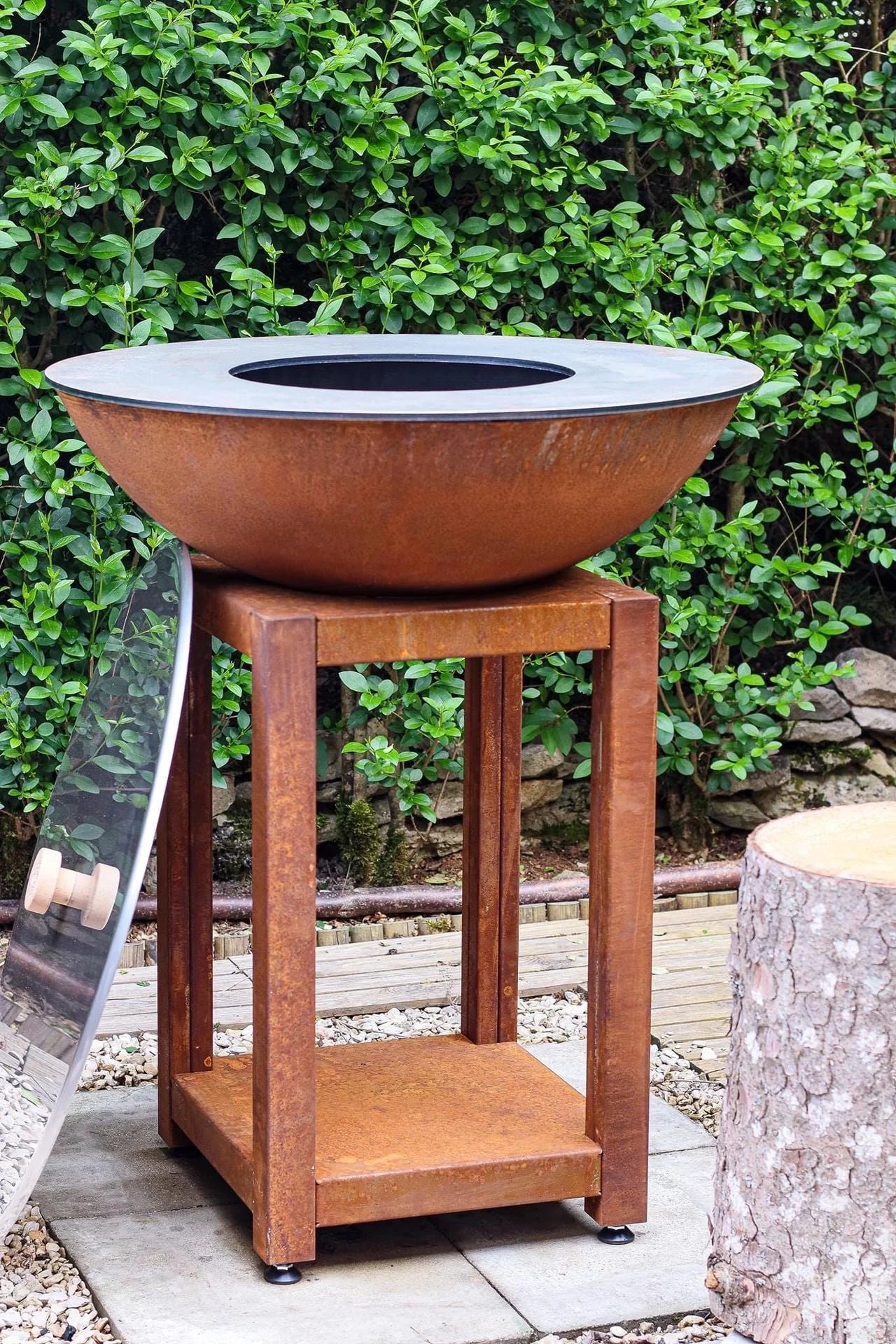 Bol en acier rouillé de couleur cuivre avec un couvercle plat gris foncé reposant sur un support en bois assorti.