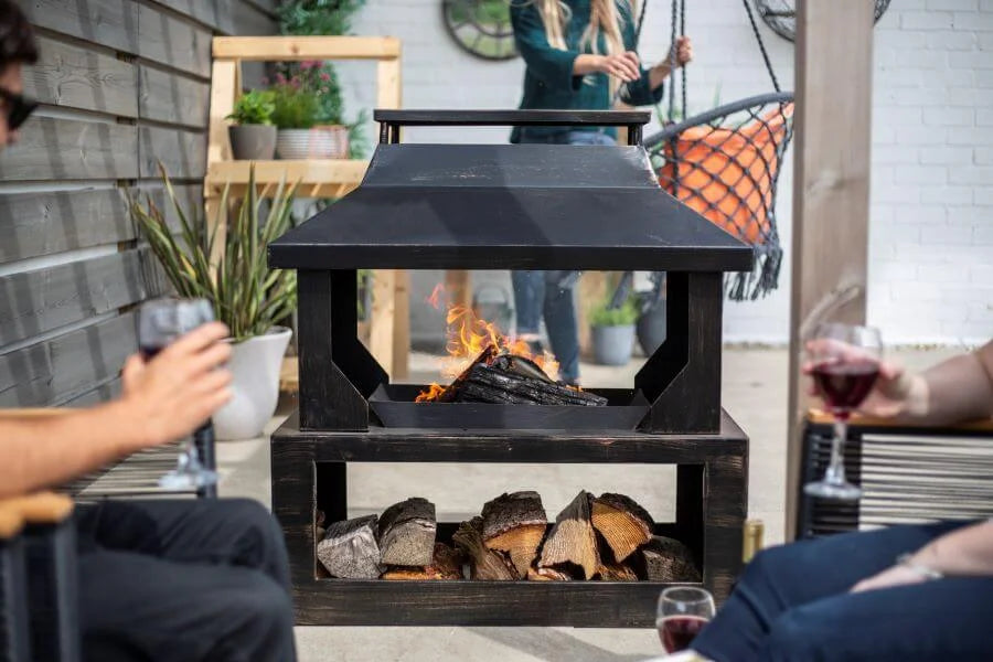 Foyer de feu en métal noir avec un toit et un compartiment de rangement inférieur rempli de bûches