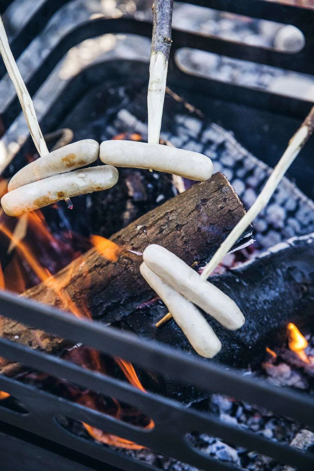 Brochettes de saucisses blanches sur la grille du foyer de barbecue.