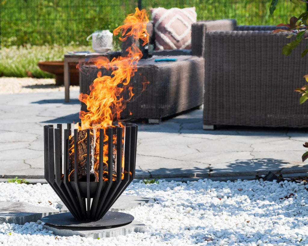 Foyer de feu en métal noir avec des lattes verticales et une base circulaire, flammes brûlant vivement à l’intérieur