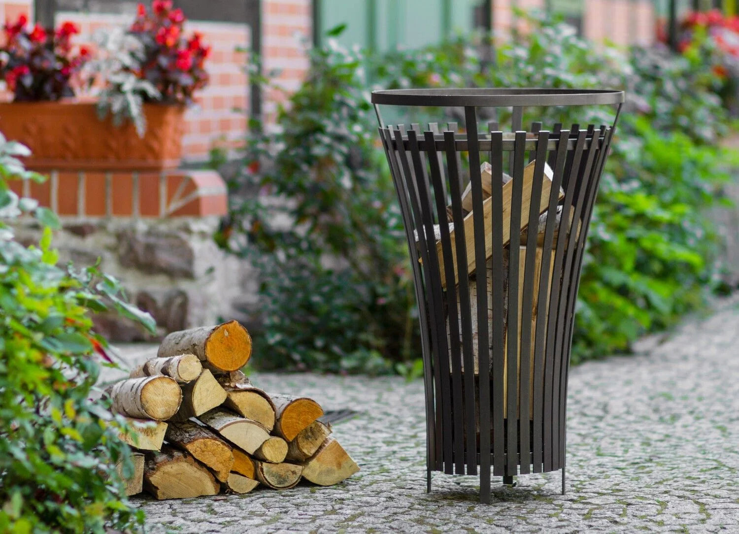 Porte-bûches en métal noir avec design ajouré et quatre pieds.