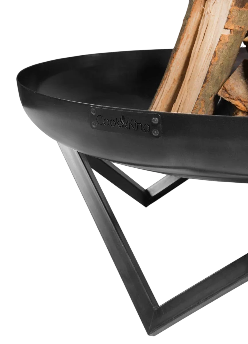 Foyer de feu en métal noir avec des jambes croisées et du bois à l’intérieur.