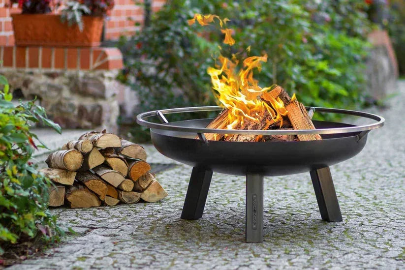 Foyer d’incendie noir avec trois pieds et un rebord en métal, conçu pour un usage extérieur.