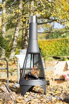 Chiminea en métal noir avec une cheminée argentée et un écran en maille, présentant des bûches qui brûlent à l’intérieur.