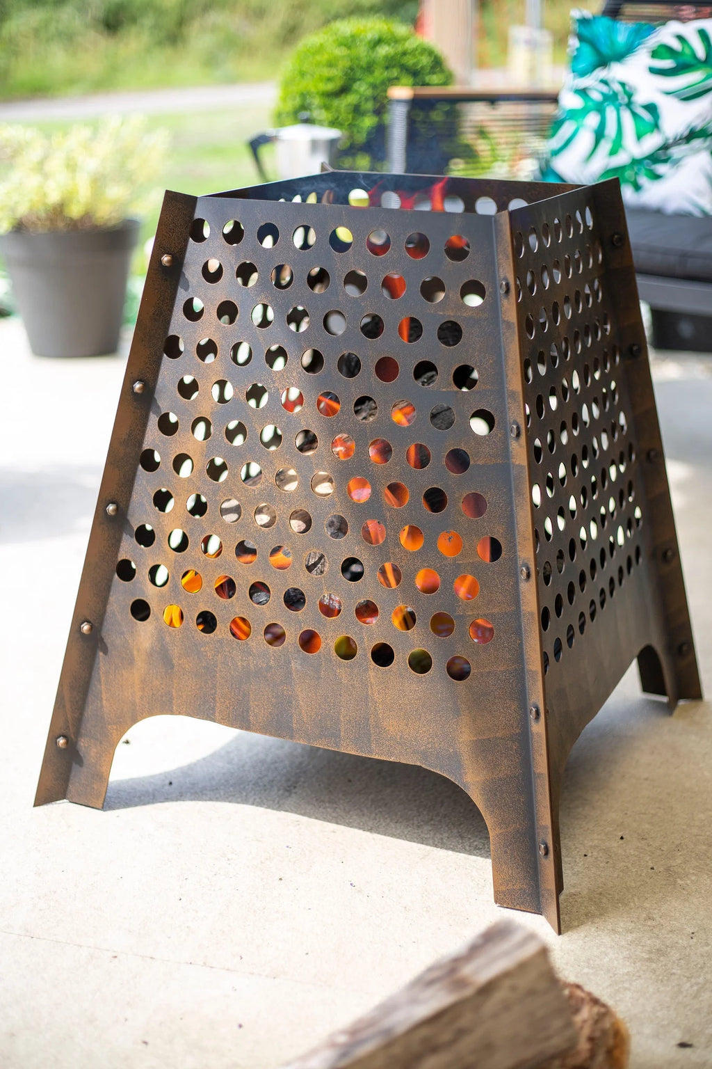 Un foyer de feu en métal bronze foncé rustique avec un design géométrique comportant des découpes circulaires espacées uniformément et des rivets visibles le long de ses bords.