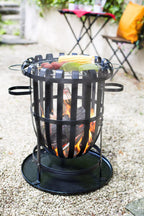 Foyer de feu en fer forgé noir avec un gril circulaire en haut retenant du maïs et des légumes au-dessus de braises rougeoyantes.