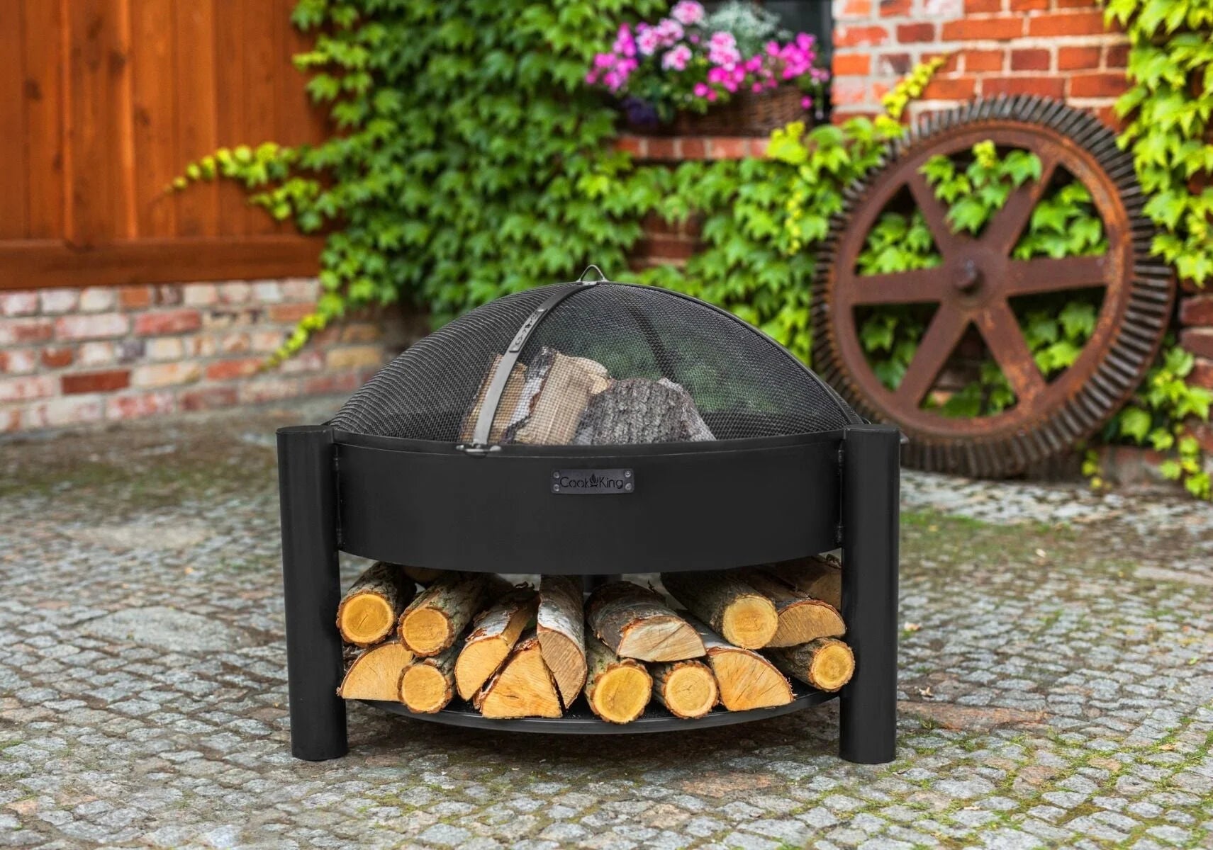Foyer de feu noir avec rangement pour bois et couvercle en maille, usage extérieur.