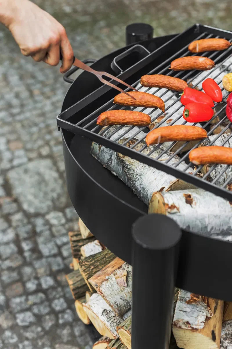 Barbecue au charbon avec cadre et grille en métal noir, contenant des saucisses et des poivrons.