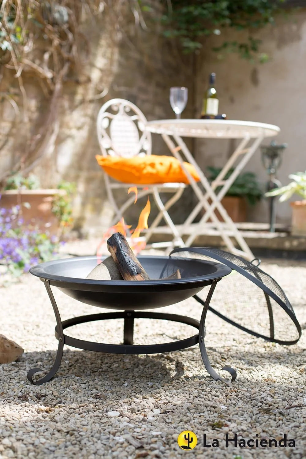 Foyer d’extérieur en fer forgé noir avec des pieds courbés et un couvercle en maille posé à côté