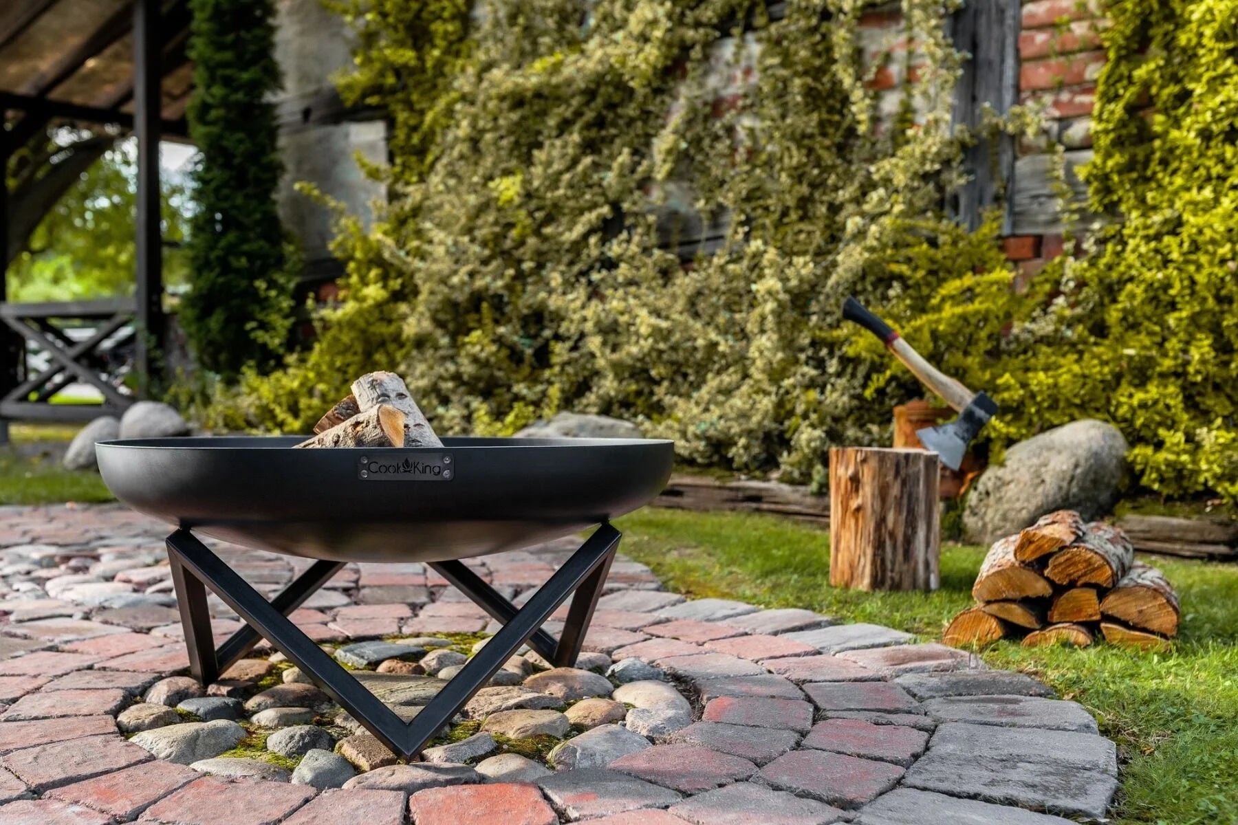 Foyer de feu en métal noir avec des pieds en forme de X et un design en bol.