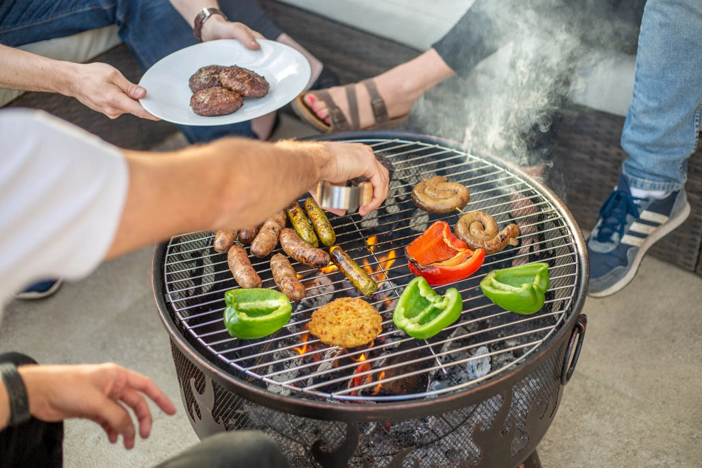 Gril rond en métal noir avec des braises incandescentes et une grille en fil de fer supportant des saucisses, des poivrons et des burgers