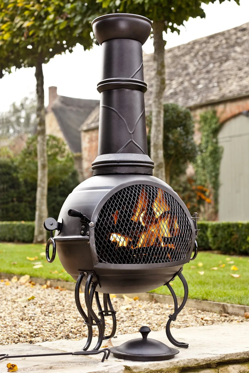 Chimenea en fonte forgée noire avec un corps arrondi, panneau avant en maille révélant les braises incandescentes à l’intérieur.