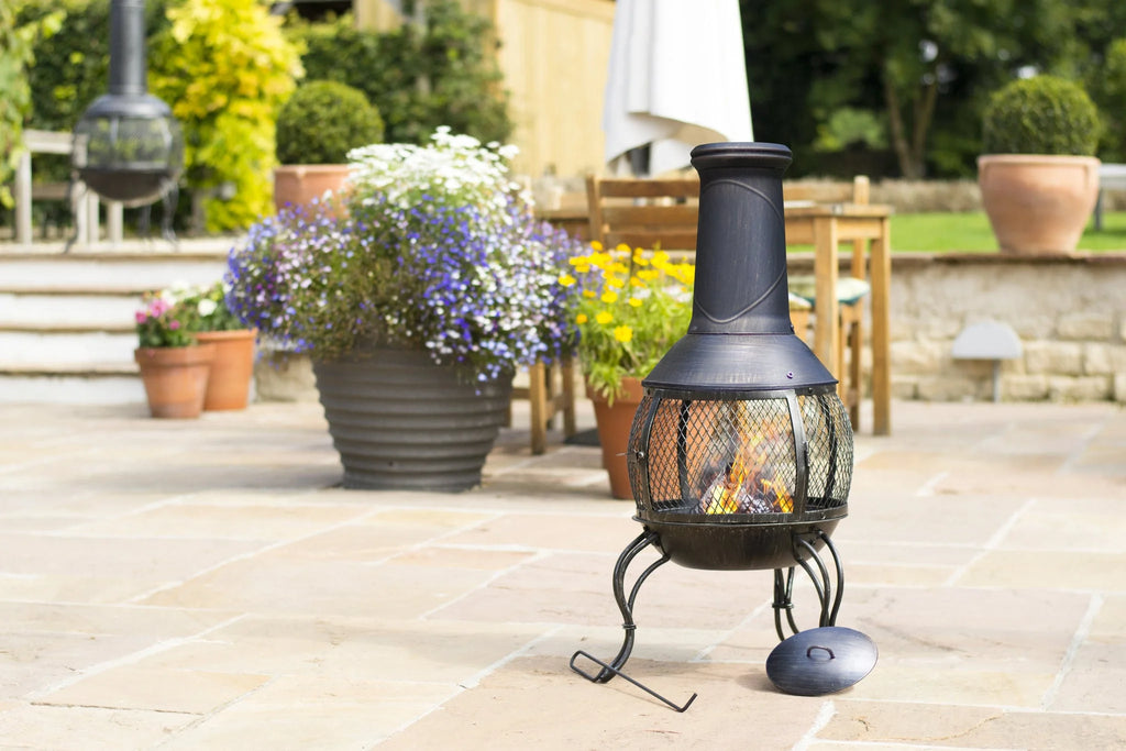 Chimenea en fonte noire forgée avec un écran en maille et une flamme à l’intérieur, reposant sur trois pieds courbés.