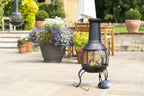 Chimenea en fonte noire forgée avec un écran en maille et une flamme à l’intérieur, reposant sur trois pieds courbés.