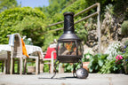 Chimenea en métal noir avec un devant en maille et une base à trois pieds, ornée d’un pied sphérique.