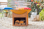 Foyer de feu en acier orange rouillé avec un dessus courbé et des bûches empilées à l’intérieur