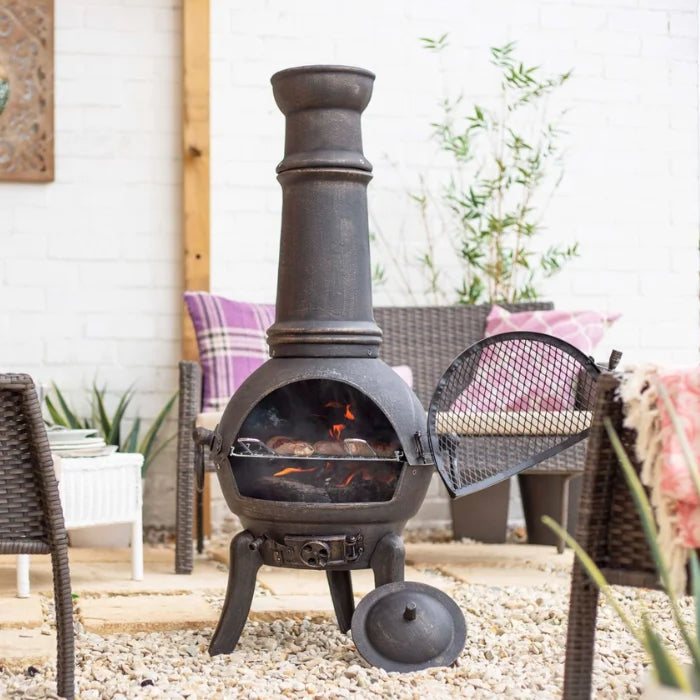 Chimenea en fonte forgée noire avec une cheminée haute et une porte en filet, présentant un corps rond sur trois pieds et un couvercle détachable à proximité.