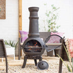 Chimenea en fonte forgée noire avec une cheminée haute et une porte en filet, présentant un corps rond sur trois pieds et un couvercle détachable à proximité.