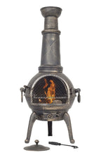 Chimenea en fonte de style ancien avec une finition grise patinée, ornée de motifs décoratifs en damier sur sa cheminée et munie de solides pieds trépied.