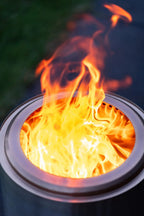 Une flamme orange et jaune vibrante danse à l’intérieur d’un foyer de feu en métal cylindrique et élégant.