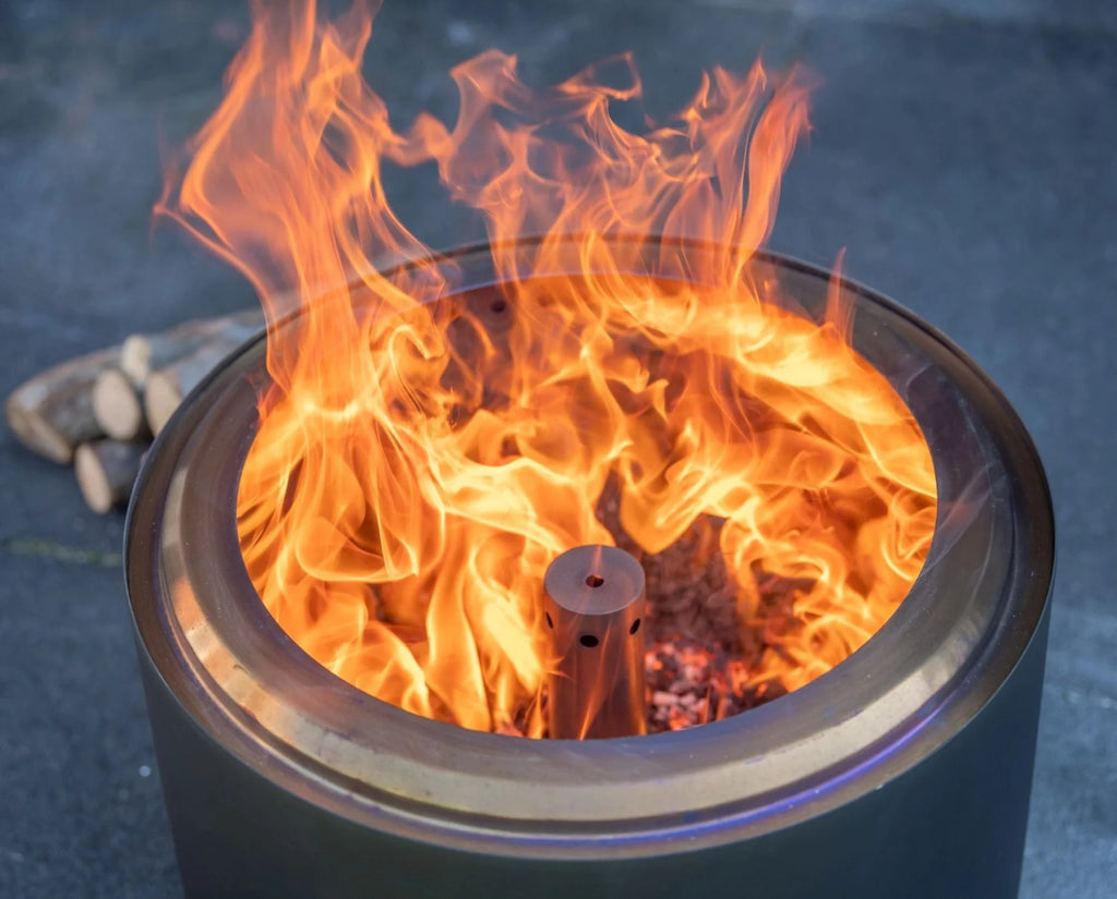 Un foyer de feu cylindrique en métal gris foncé avec une flamme orange luisante qui danse à l’intérieur et un brûleur central.