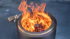 Un foyer de feu métallique cylindrique élégant avec une flamme orange vibrante dansant à l’intérieur de son ouverture circulaire.