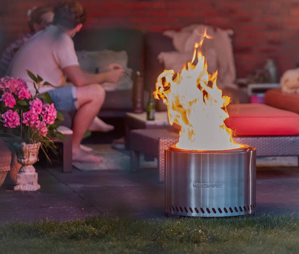 Un foyer de feu en acier inoxydable cylindrique et élégant avec une flamme vive brûlant à l’intérieur et le nom de marque ’redfire’ gravé sur son côté.