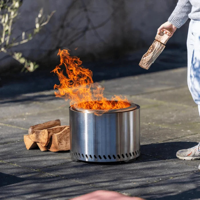 Foyer de feu cylindrique en acier inoxydable avec un design élégant et moderne et des fentes de ventilation autour de la base.