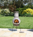 Chimenea en terracota avec des motifs blancs gravés complexes et un feu orange luminescent à l’intérieur, reposant sur des pieds en métal noir.