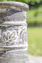Pot en céramique gris patiné avec motifs de feuilles en relief et une finition rustique usée.