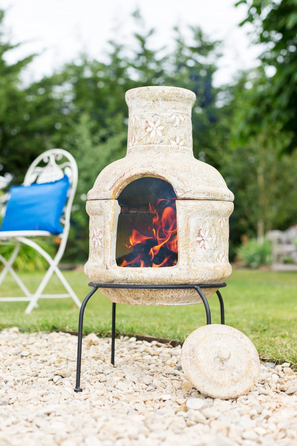 Chimenea en pierre avec motifs floraux sculptés et un support en métal noir, présentant une ouverture arquée révélant des braises incandescentes à l’intérieur.