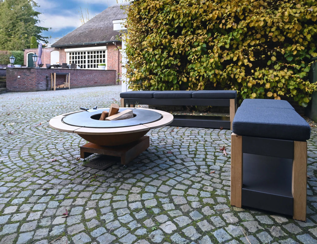 Foyer de feu rond moderne avec un bol de couleur bronze et un dessus circulaire noir, posé sur une base en bois.