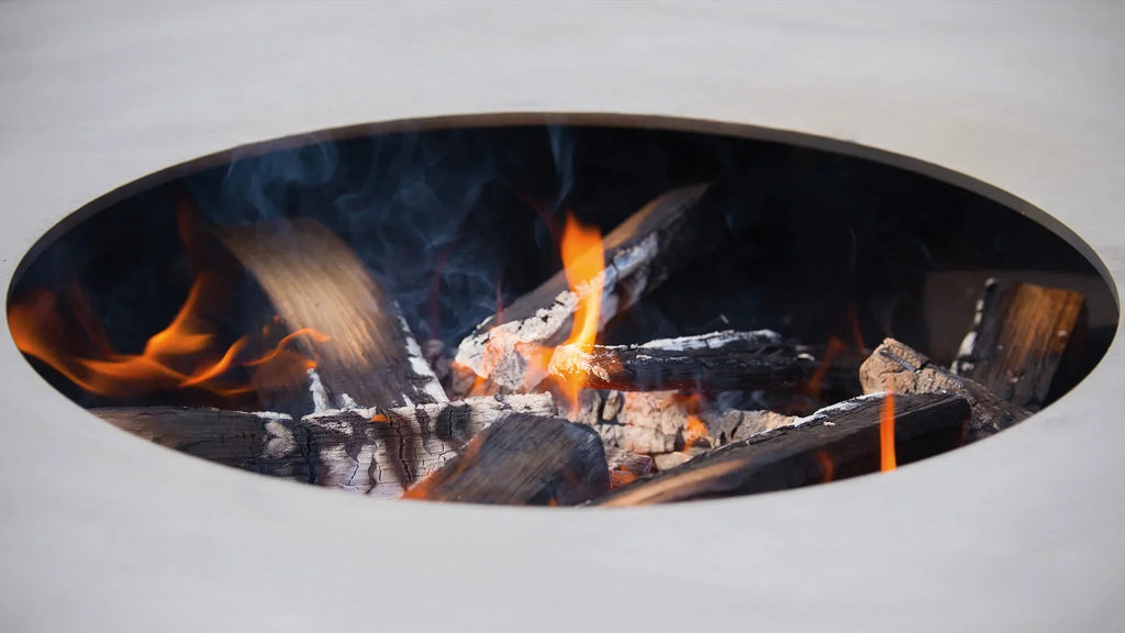 Un insert de cheminée ovale blanc moderne avec un feu brillant qui brûle à l’intérieur, comportant des bûches et des braises.