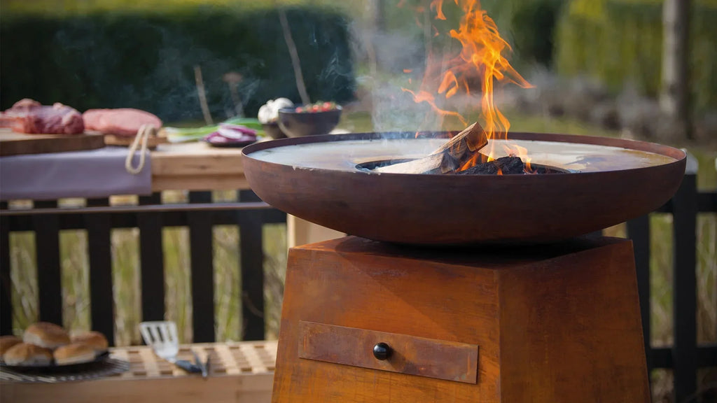 Bol d’incendie en acier brun rouillé avec une flamme brûlant à l’intérieur, reposant sur une base de piédestal assortie