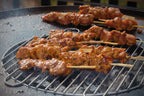 Brochettes de poulet grillées avec un glaçage brillant et caramélisé qui grésille sur du charbon dans un gril rond.