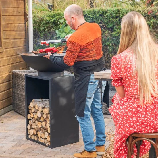 Grill extérieur en fonte noire avec un design moderne élégant et un espace de rangement intégré pour bûches de bois.