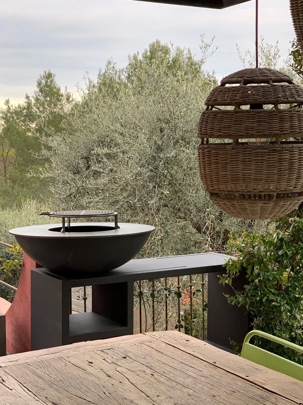 Bol en fonte noire pour feu de camp avec une grille métallique circulaire sur le dessus, reposant sur un support noir moderne.