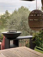 Bol en fonte noire pour feu de camp avec une grille métallique circulaire sur le dessus, reposant sur un support noir moderne.