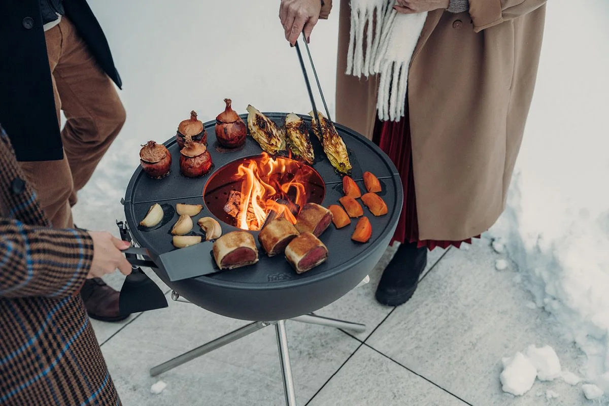 Foyer de feu rond noir avec des flammes et des aliments sur des brochettes.