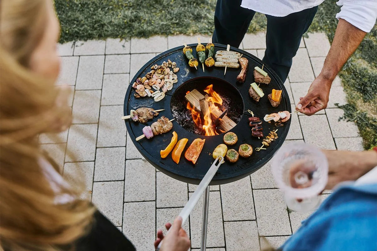Gril rond noir avec des flammes et des aliments sur des brochettes.